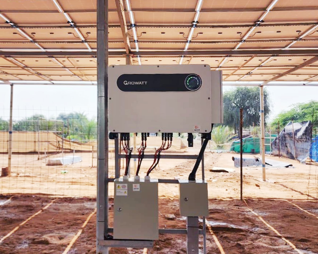 A Growatt solar inverter mounted on a metal frame inside a sunlit agricultural structure with a sandy floor and distant green foliage, How Solar Inverters Efficiently Manage High-Temperature Condit